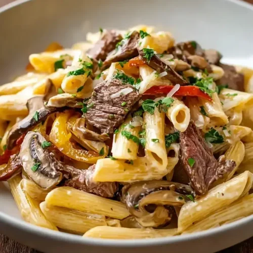 Philly Cheesesteak Pasta in a white bowl with melted cheese and peppers.