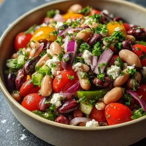 Dense bean salad recipe in a rustic bowl with colorful veggies and vegan feta.