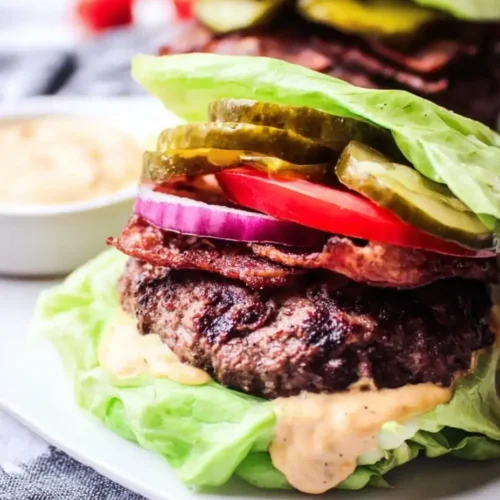 Keto burger recipe wrapped in lettuce with beef patty, bacon, pickles, tomato, and sauce